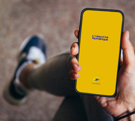 Une main tient un téléphone portable sur lequel on voit l'application L'Identité Numérique se lancer.