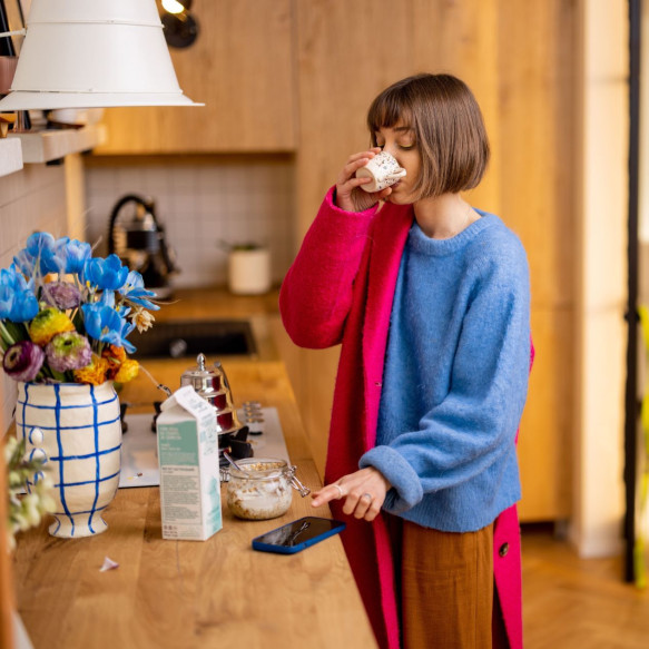 Une femme dans la cuisine dirige sa main vers son téléphone portable